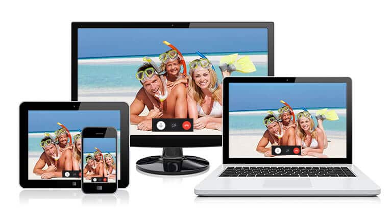 Geräte für Videotelefonie: Ein PC-Bildschirm, ein Laptop, ein Tablet und ein Smartphone, auf denen ein Videoanruf mit der Familie läuft, die am Strand liegt und in die Kamera lacht.
